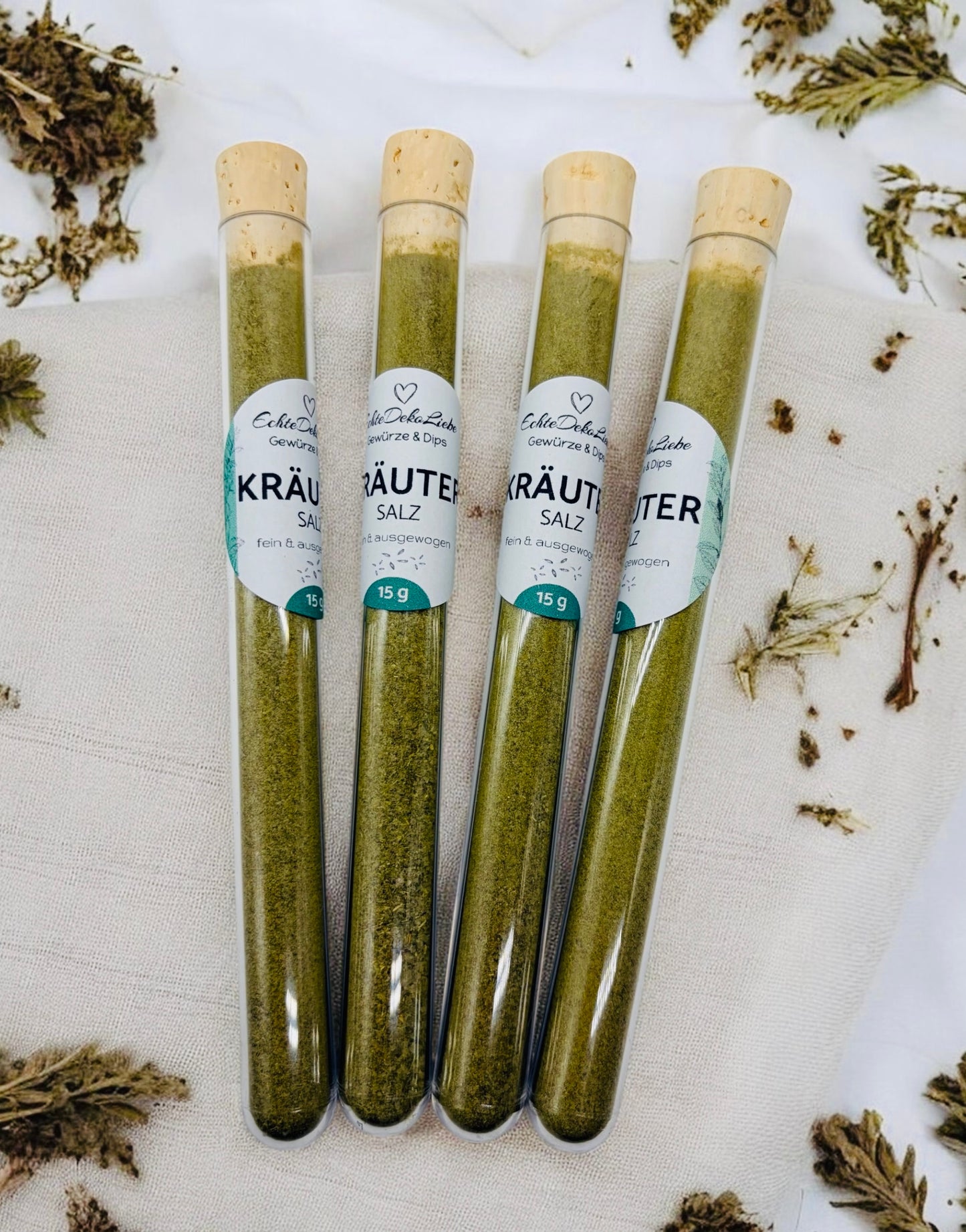 Sieben Reagenzgläser mit Naturkorken, gefüllt mit verschiedenen Gewürzen und Salzen. Zu sehen sind Rühreigewürz, Kräutersalz, Himalayasalz, Pommesgewürz, Aglio-Olio-Gewürz, vergoldeter Pfeffer und vergoldetes Salz. Die Gläser tragen moderne weiße Etiketten mit Produktname und Füllmenge. Arrangiert auf hellem Holzhintergrund mit dekorativen Trockenblumen – eine besondere Geschenkidee für Gewürzliebhaber.