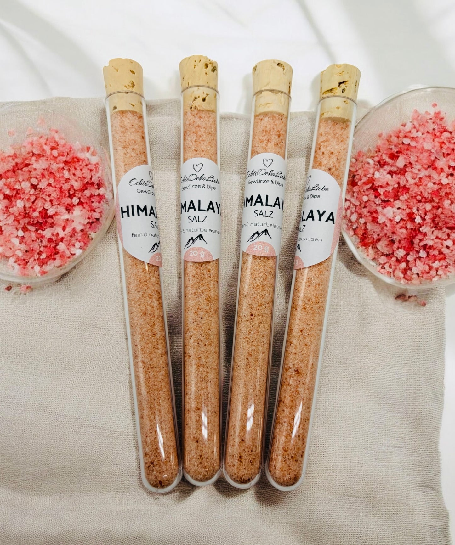 Sieben Reagenzgläser mit Naturkorken, gefüllt mit verschiedenen Gewürzen und Salzen. Zu sehen sind Rühreigewürz, Kräutersalz, Himalayasalz, Pommesgewürz, Aglio-Olio-Gewürz, vergoldeter Pfeffer und vergoldetes Salz. Die Gläser tragen moderne weiße Etiketten mit Produktname und Füllmenge. Arrangiert auf hellem Holzhintergrund mit dekorativen Trockenblumen – eine besondere Geschenkidee für Gewürzliebhaber.