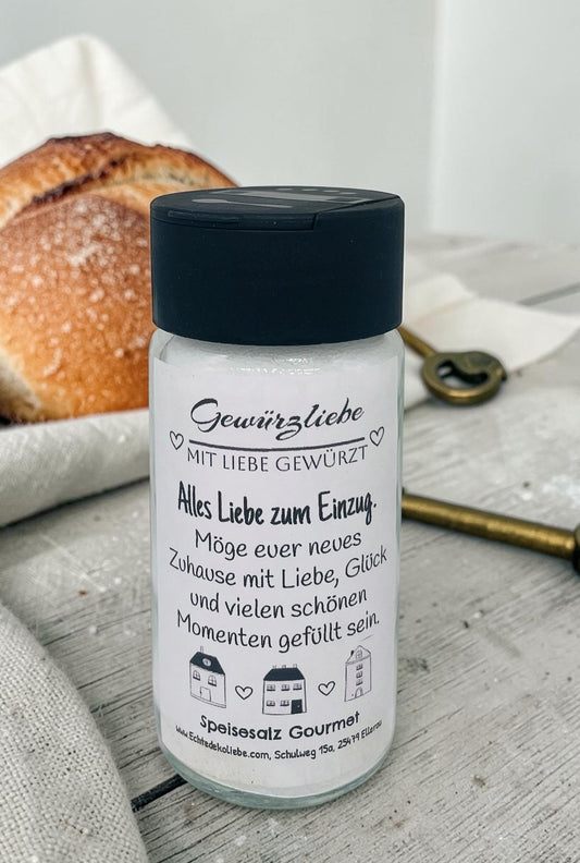 Ein hochwertiges Glas mit Speisesalz Gourmet und einem liebevoll gestalteten Etikett im modernen Schwarz-Weiß-Design. Oben steht „Gewürzliebe – Mit Liebe gewürzt“, darunter „Alles Liebe zum Einzug“ sowie der Spruch „Möge euer neues Zuhause mit Liebe, Glück und vielen schönen Momenten gefüllt sein.“ Im unteren Bereich sind kleine gezeichnete Häuser abgebildet. Das Glas eignet sich als stilvolles Einzugsgeschenk oder Mitbringsel für das neue Zuhause.
