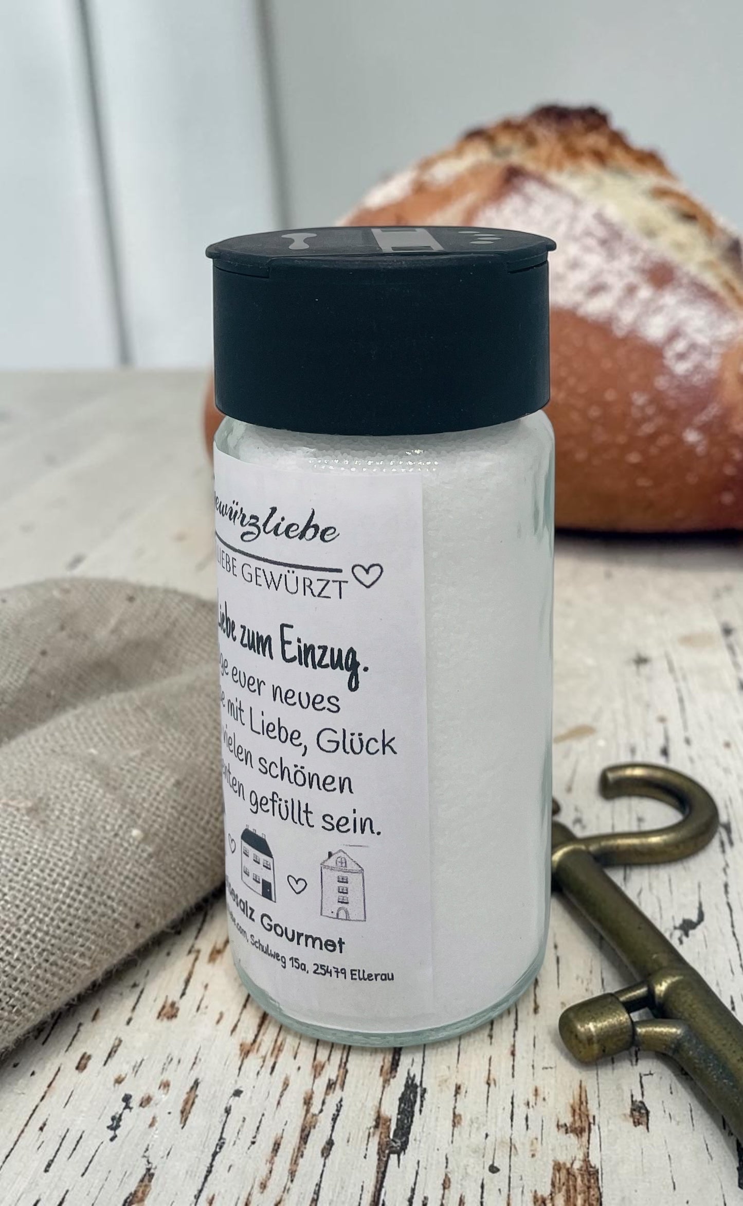 Ein hochwertiges Glas mit Speisesalz Gourmet und einem liebevoll gestalteten Etikett im modernen Schwarz-Weiß-Design. Oben steht „Gewürzliebe – Mit Liebe gewürzt“, darunter „Alles Liebe zum Einzug“ sowie der Spruch „Möge euer neues Zuhause mit Liebe, Glück und vielen schönen Momenten gefüllt sein.“ Im unteren Bereich sind kleine gezeichnete Häuser abgebildet. Das Glas eignet sich als stilvolles Einzugsgeschenk oder Mitbringsel für das neue Zuhause.