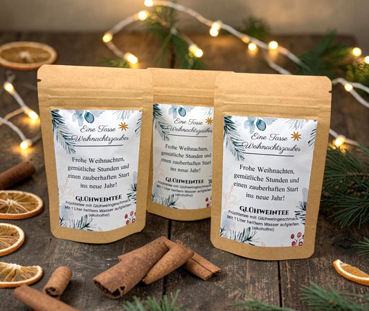 Braune Kraftpapiertüten mit weihnachtlichem Design stehen dekorativ auf einem rustikalen Holztisch. Die Tüten sind mit einem winterlich gestalteten Etikett versehen und enthalten eine Getränkemischung bzw. ein Heißgetränk zum Genießen. Im Hintergrund sorgen Tannenzweige, warme Lichter und weihnachtliche Dekoration für eine gemütliche Adventsstimmung.