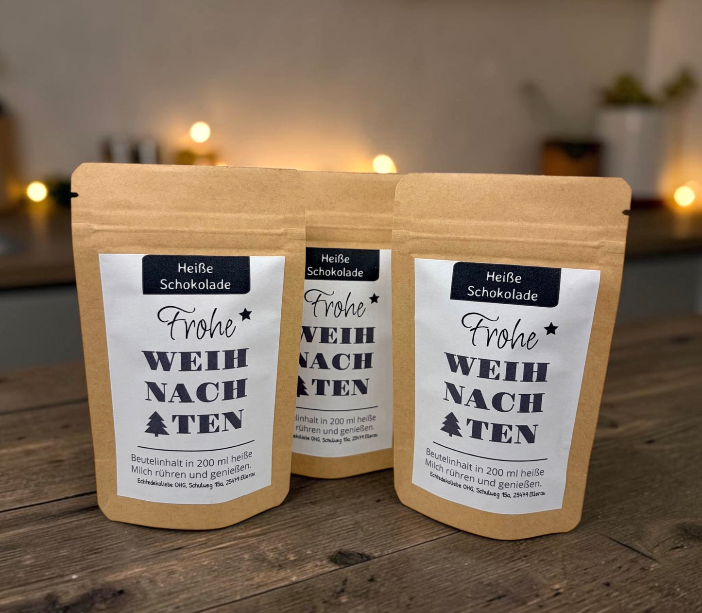 Braune Kraftpapiertüten mit weihnachtlichem Design stehen dekorativ auf einem rustikalen Holztisch. Die Tüten sind mit einem winterlich gestalteten Etikett versehen und enthalten eine Getränkemischung bzw. ein Heißgetränk zum Genießen. Im Hintergrund sorgen Tannenzweige, warme Lichter und weihnachtliche Dekoration für eine gemütliche Adventsstimmung.
