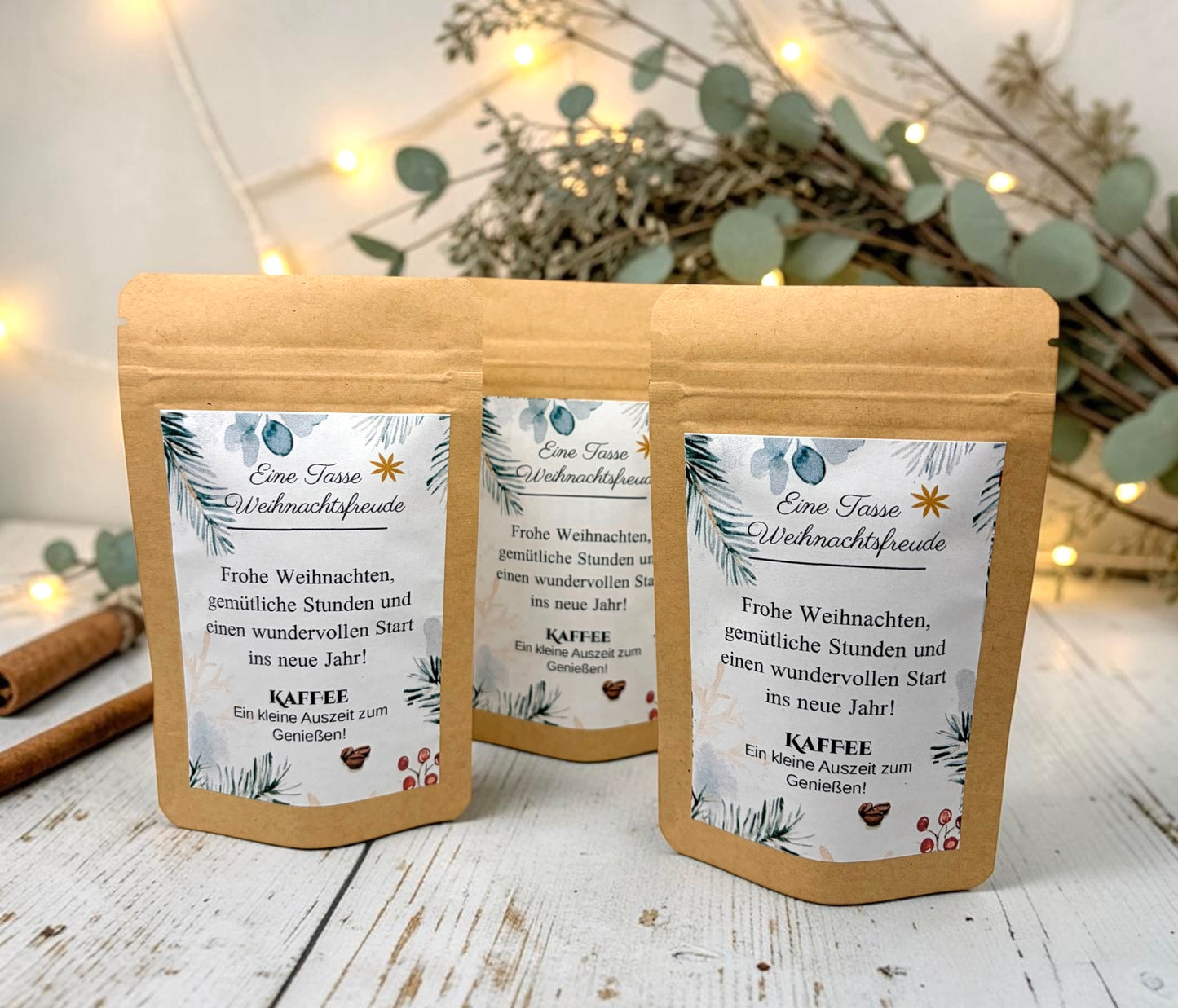 Braune Kraftpapiertüten mit weihnachtlichem Design stehen dekorativ auf einem rustikalen Holztisch. Die Tüten sind mit einem winterlich gestalteten Etikett versehen und enthalten eine Getränkemischung bzw. ein Heißgetränk zum Genießen. Im Hintergrund sorgen Tannenzweige, warme Lichter und weihnachtliche Dekoration für eine gemütliche Adventsstimmung.